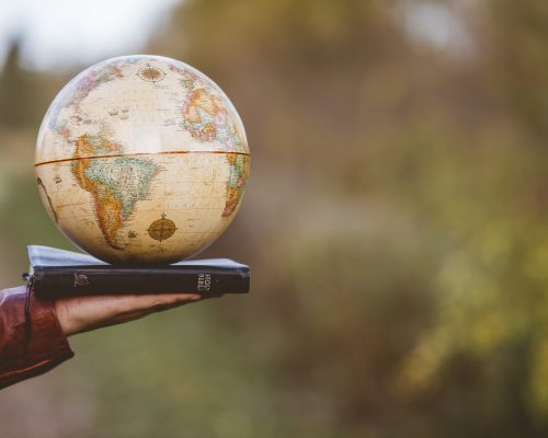 A closeup shot of a person holding bible with desk globe on top with a blurred background